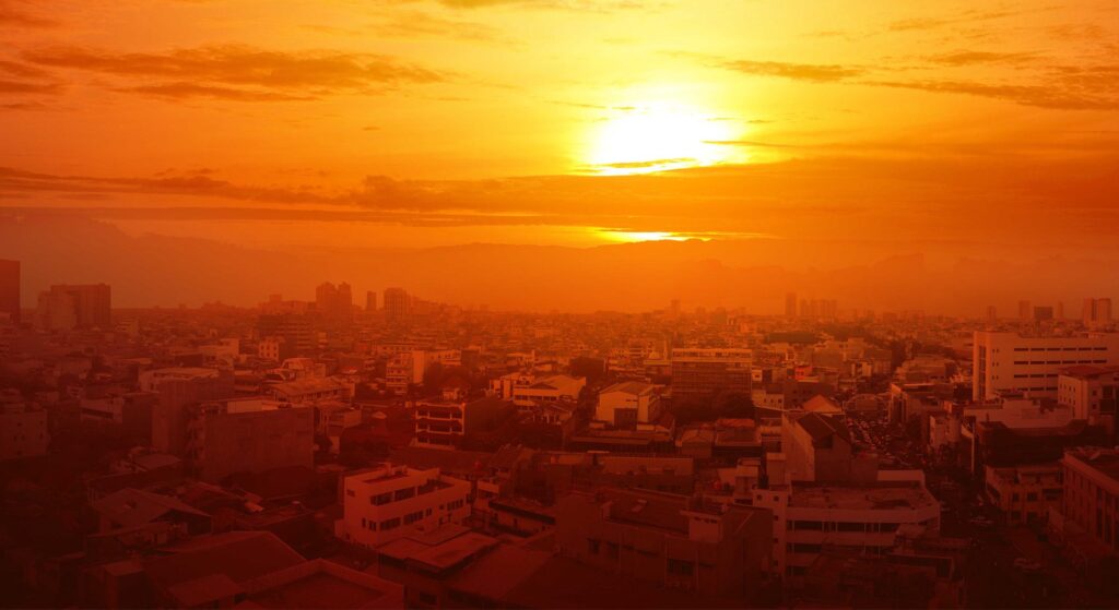 An stifling oppressive atmosphere hanging over a city, a harsh sun shining in a sky tinged with yellow haze.